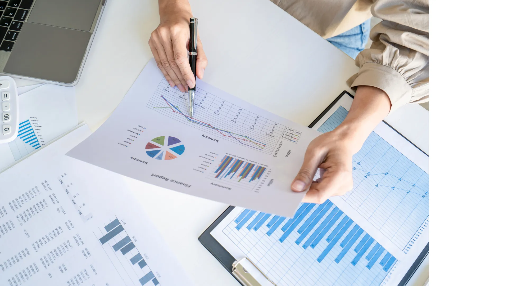 Hände analysieren ausgedruckte Diagramme und Tabellen mit Stift, darunter Balken-, Kreis- und Zeitreihendiagramme.
